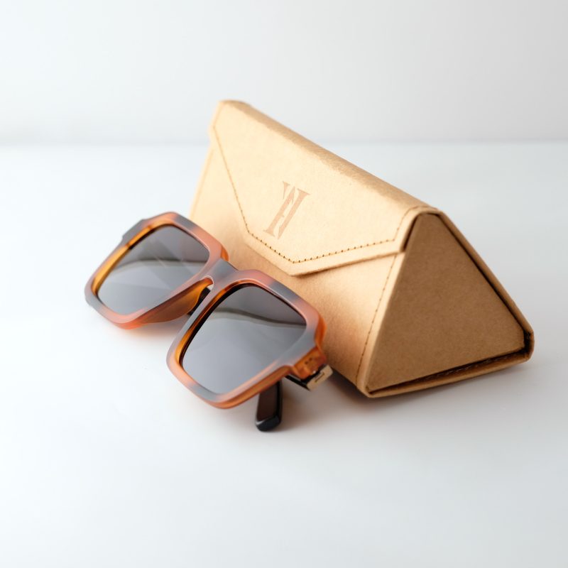 Carpatia bamboo sunglasses, folded next to case, on a white background. tortie frames, dark lenses.